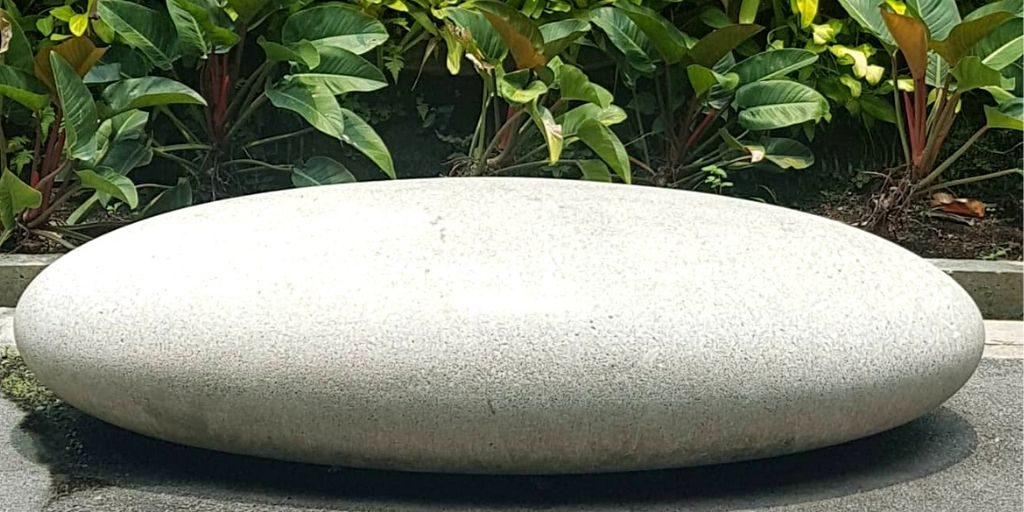 A large smooth white sculpted rock placed in front of a wall of plants