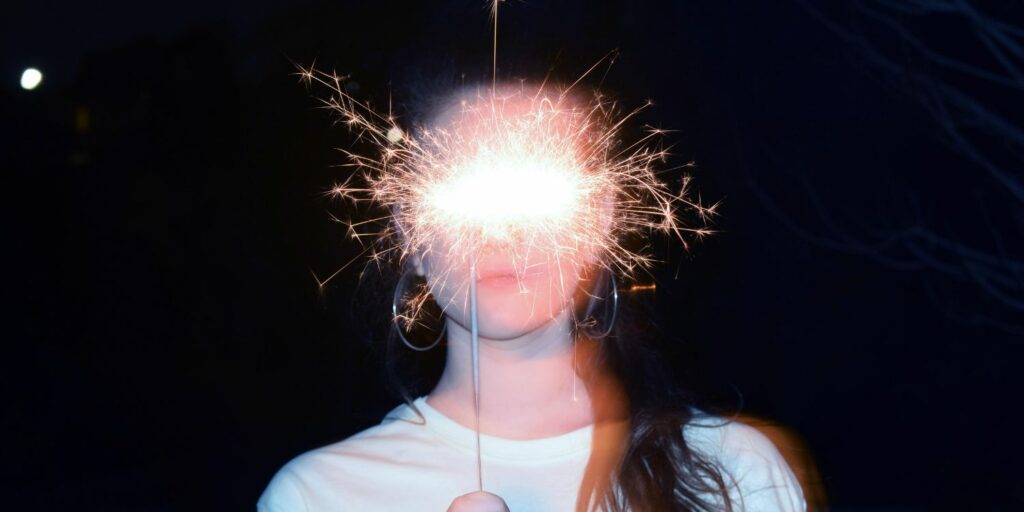 A girl standing with a sprinkler covering her eyes