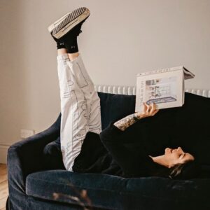 Woman lying on a couch, legs in the air reading. Photo by Toa Heftiba on UnSplash
